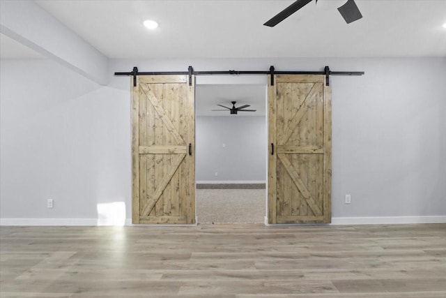 empty room with a barn door, hardwood / wood-style floors, and ceiling fan