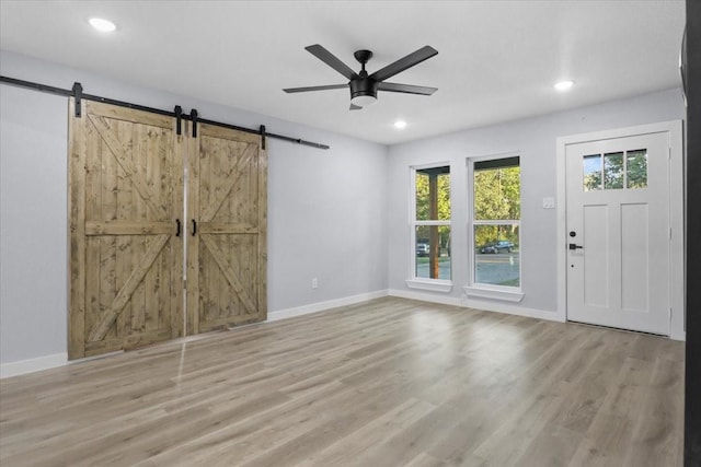 foyer with light hardwood / wood-style flooring, a barn door, and ceiling fan