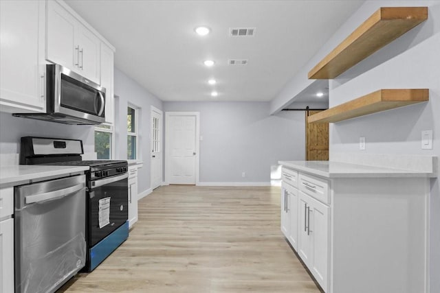 kitchen with stainless steel appliances, light stone counters, white cabinets, a barn door, and light wood-type flooring