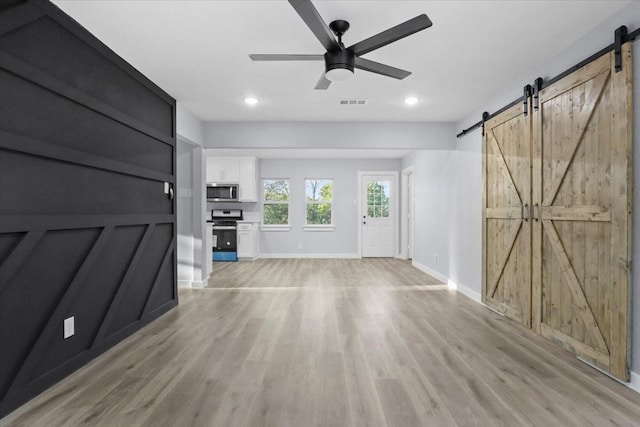 unfurnished living room with ceiling fan, a barn door, and light hardwood / wood-style floors