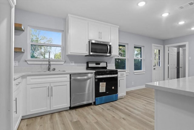 kitchen with appliances with stainless steel finishes, sink, white cabinets, and light hardwood / wood-style flooring