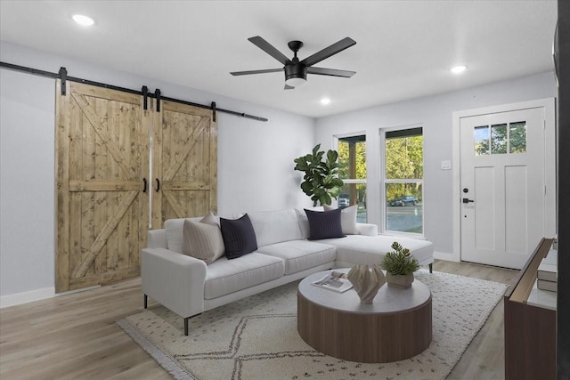 living room featuring ceiling fan, a barn door, and light hardwood / wood-style floors