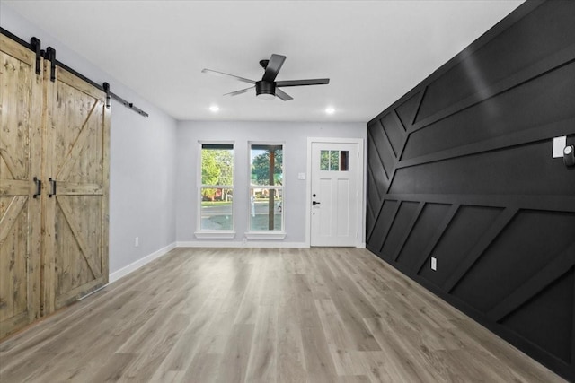 interior space with ceiling fan, a barn door, and light hardwood / wood-style flooring