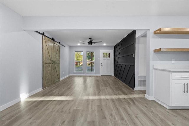 unfurnished living room with ceiling fan, a barn door, and light hardwood / wood-style floors