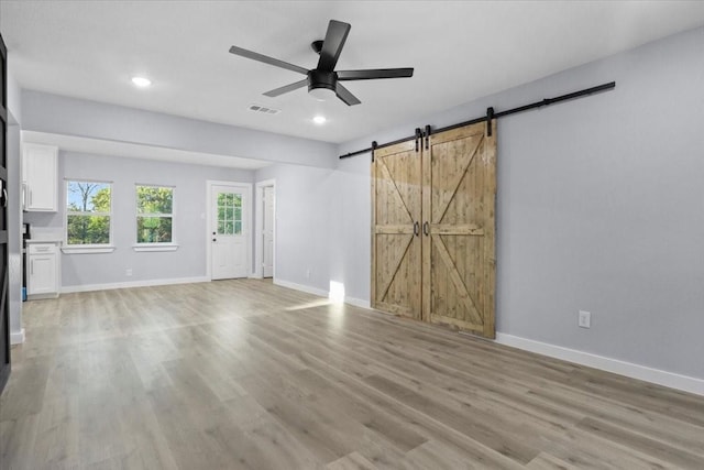 unfurnished living room with a barn door, ceiling fan, and light wood-type flooring