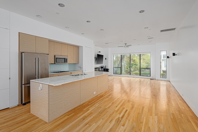 kitchen with ceiling fan, sink, a spacious island, appliances with stainless steel finishes, and light wood-type flooring