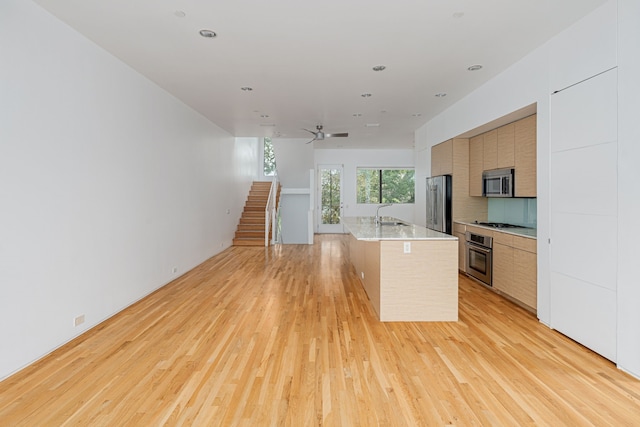 kitchen with stainless steel appliances, a kitchen island with sink, ceiling fan, light hardwood / wood-style flooring, and a breakfast bar area