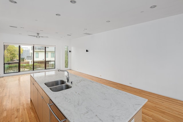 kitchen featuring light stone counters, stainless steel dishwasher, sink, light hardwood / wood-style flooring, and an island with sink