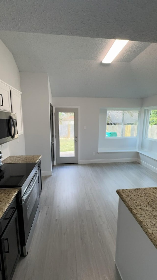 kitchen with white cabinetry, light stone counters, light hardwood / wood-style floors, a textured ceiling, and appliances with stainless steel finishes