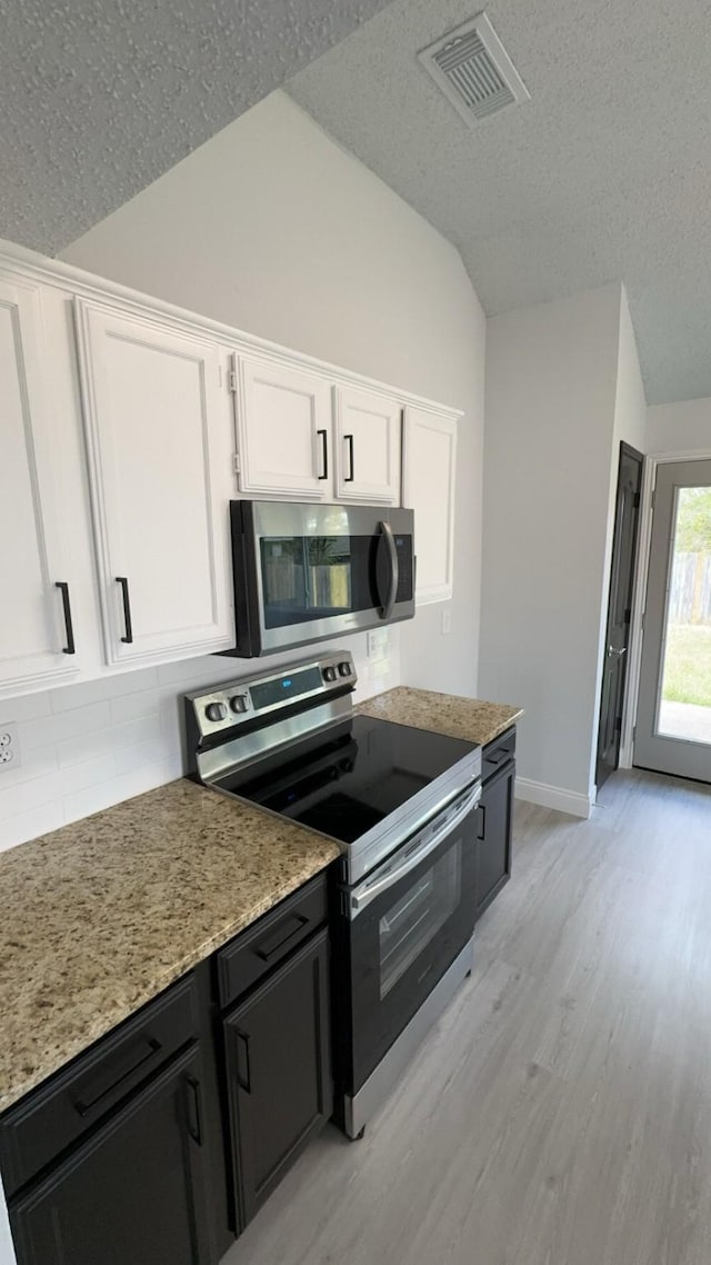 kitchen featuring white cabinets, appliances with stainless steel finishes, a textured ceiling, and lofted ceiling