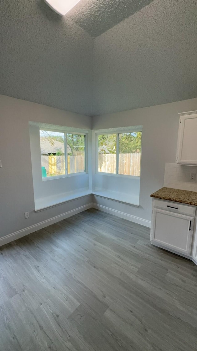 unfurnished dining area with lofted ceiling, light wood-type flooring, and a textured ceiling