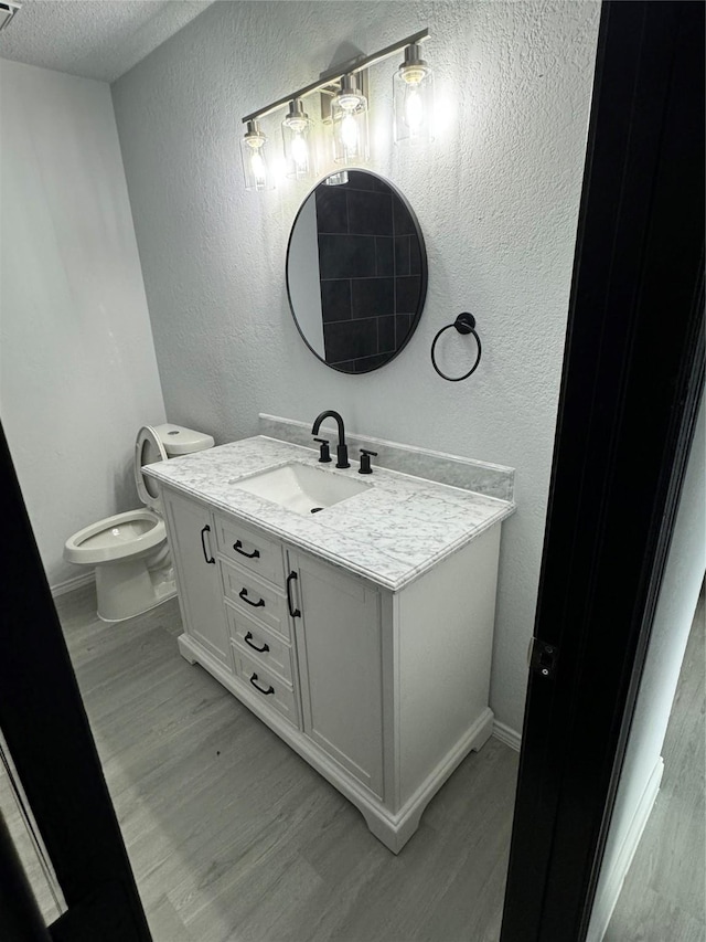 bathroom featuring hardwood / wood-style flooring, vanity, toilet, and a textured ceiling