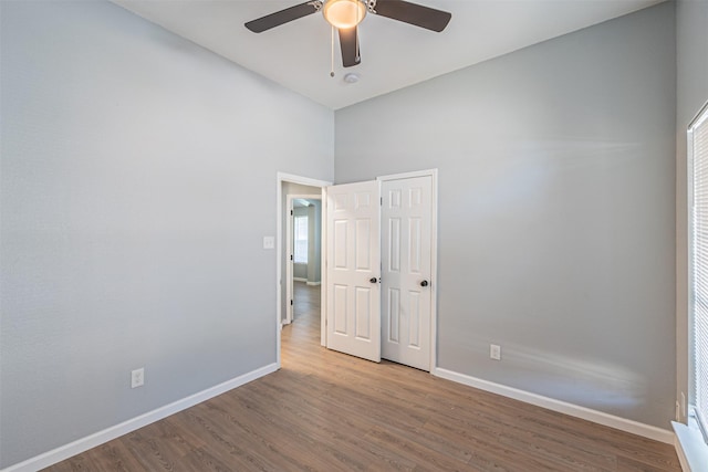 empty room with wood-type flooring, a towering ceiling, and ceiling fan