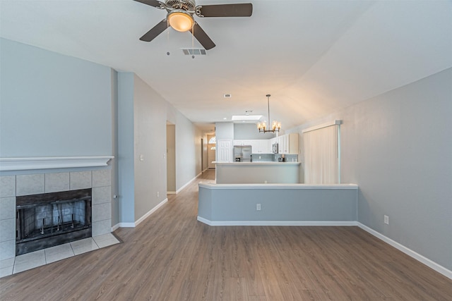 unfurnished living room with hardwood / wood-style flooring, ceiling fan with notable chandelier, a tiled fireplace, and vaulted ceiling