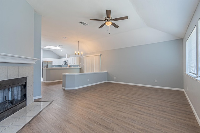 unfurnished living room featuring a tile fireplace, ceiling fan with notable chandelier, light hardwood / wood-style floors, and lofted ceiling