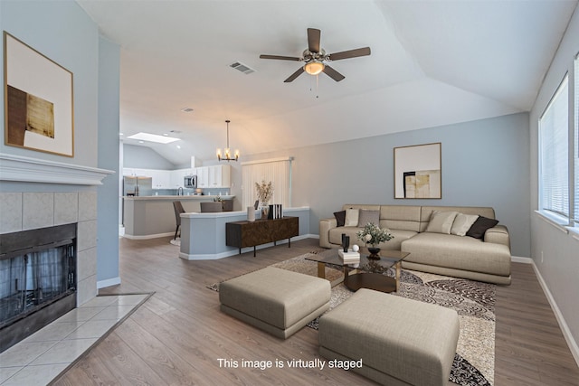 living room with a fireplace, ceiling fan with notable chandelier, lofted ceiling, and light wood-type flooring