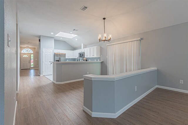 kitchen with kitchen peninsula, vaulted ceiling with skylight, light wood-type flooring, appliances with stainless steel finishes, and white cabinetry