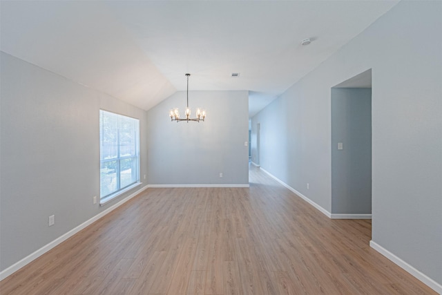 empty room with a notable chandelier, vaulted ceiling, and light hardwood / wood-style flooring