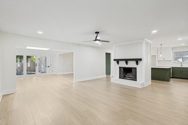 unfurnished living room featuring a fireplace, light hardwood / wood-style flooring, ceiling fan, and sink