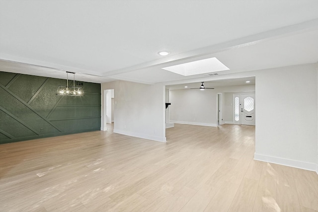 empty room featuring ceiling fan with notable chandelier, light hardwood / wood-style floors, and a skylight