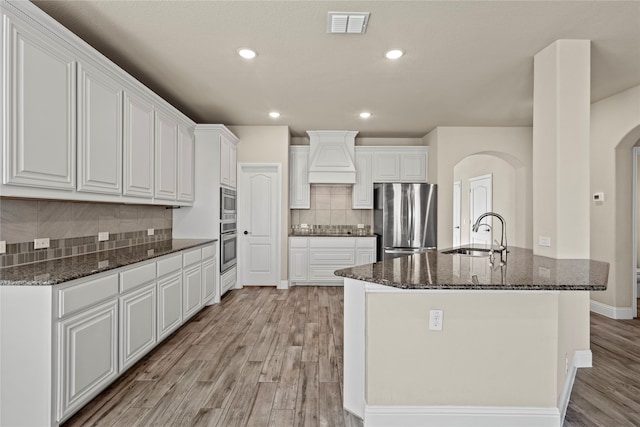 kitchen featuring stainless steel appliances, sink, light hardwood / wood-style flooring, dark stone countertops, and white cabinetry