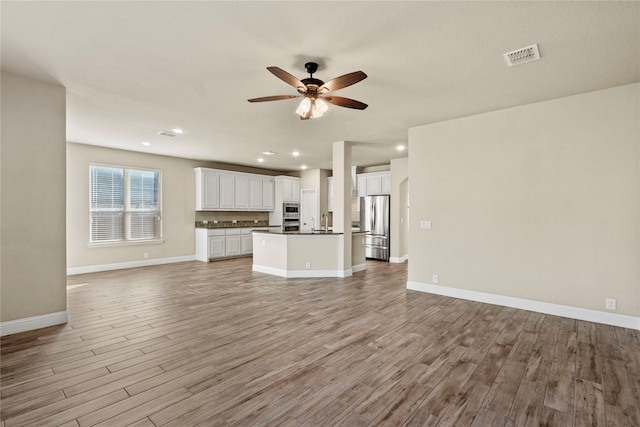 unfurnished living room featuring ceiling fan, sink, and light wood-type flooring