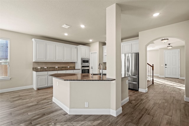 kitchen featuring light wood-type flooring, backsplash, stainless steel appliances, dark stone countertops, and white cabinets