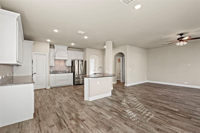 kitchen with stainless steel fridge, light wood-type flooring, premium range hood, sink, and white cabinets