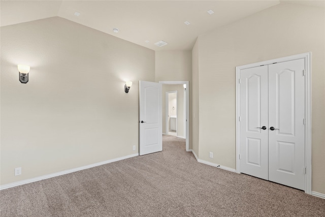 unfurnished bedroom with light carpet, a closet, and lofted ceiling