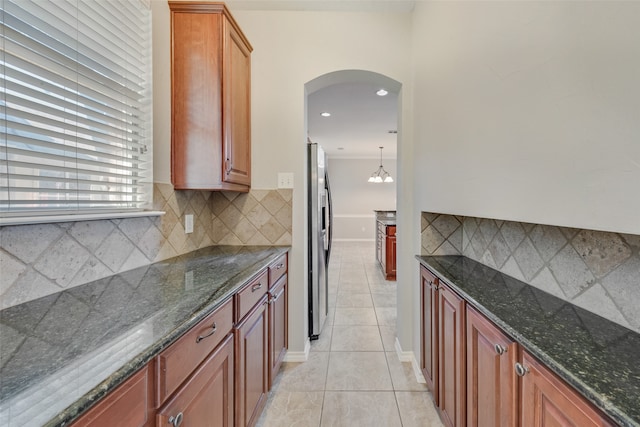 kitchen with tasteful backsplash, stainless steel fridge with ice dispenser, dark stone counters, decorative light fixtures, and light tile patterned floors