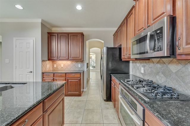 kitchen featuring crown molding, light tile patterned floors, dark stone counters, and appliances with stainless steel finishes