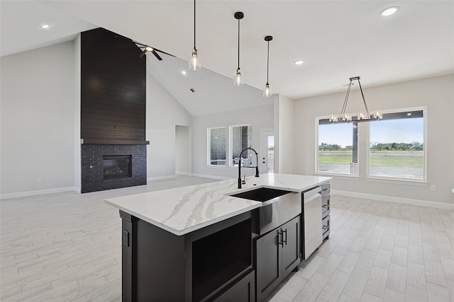 kitchen featuring a brick fireplace, stainless steel dishwasher, sink, decorative light fixtures, and an island with sink