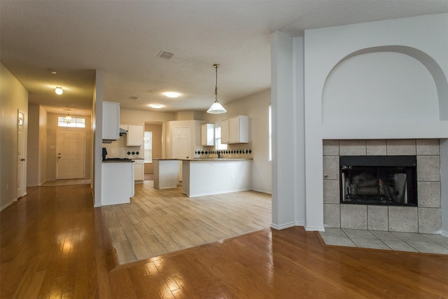 kitchen with white cabinets, light wood-type flooring, decorative light fixtures, and a fireplace