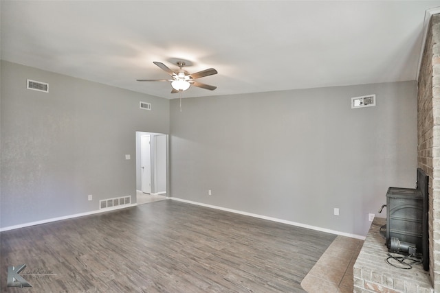 unfurnished living room featuring a wood stove, ceiling fan, and dark hardwood / wood-style flooring