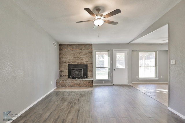 unfurnished living room featuring hardwood / wood-style floors, a wood stove, and ceiling fan