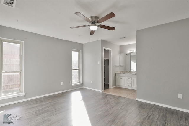 unfurnished bedroom featuring ensuite bath, ceiling fan, a spacious closet, a closet, and light wood-type flooring