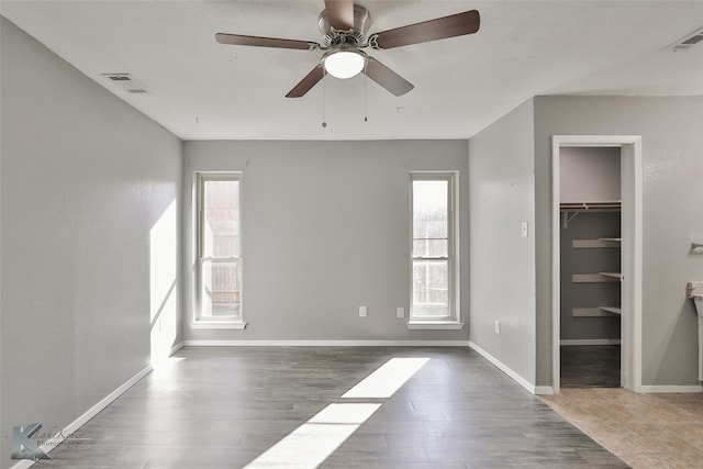 unfurnished bedroom with a closet, a spacious closet, hardwood / wood-style floors, and ceiling fan