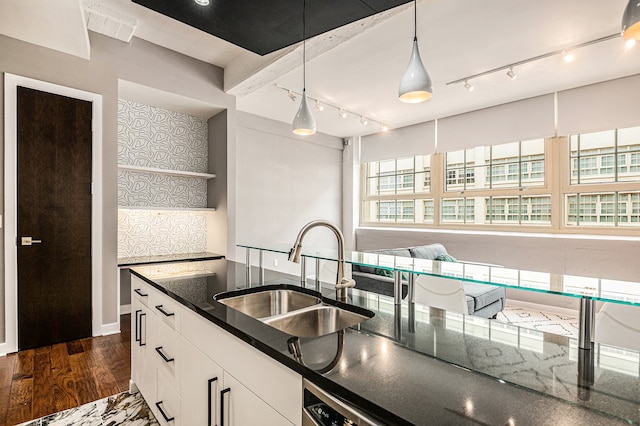 kitchen with dark wood-type flooring, dark stone counters, white cabinets, hanging light fixtures, and sink