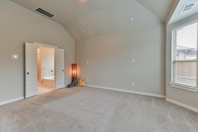 unfurnished bedroom with connected bathroom, light colored carpet, vaulted ceiling, and multiple windows