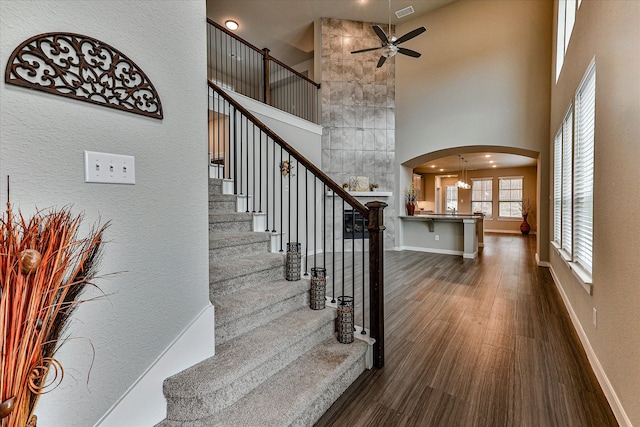 stairs with ceiling fan with notable chandelier, wood-type flooring, and a high ceiling