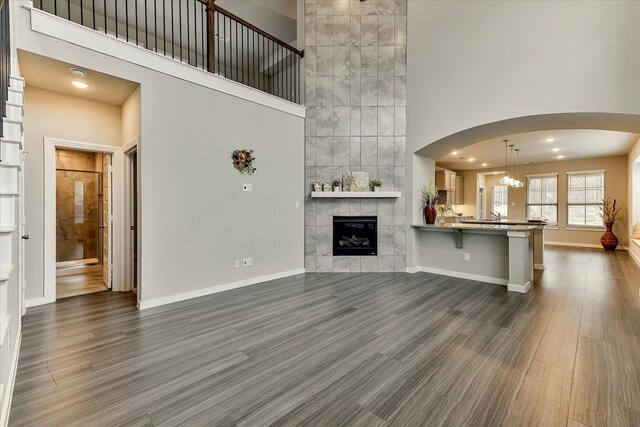 unfurnished living room featuring a fireplace, a high ceiling, dark hardwood / wood-style flooring, and ceiling fan with notable chandelier