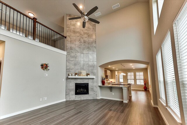 unfurnished living room with a tiled fireplace, tile walls, wood-type flooring, and a high ceiling