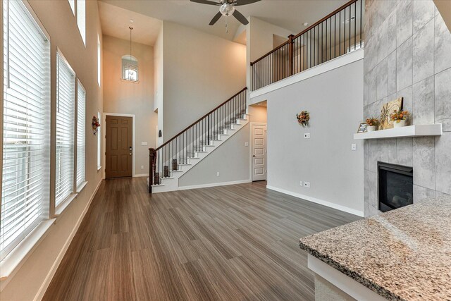 living room with ceiling fan, a fireplace, a towering ceiling, and dark hardwood / wood-style floors