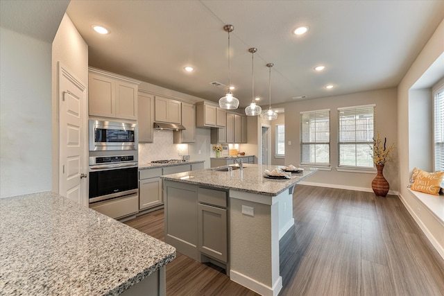 kitchen with gray cabinetry, light stone countertops, hanging light fixtures, dark wood-type flooring, and appliances with stainless steel finishes