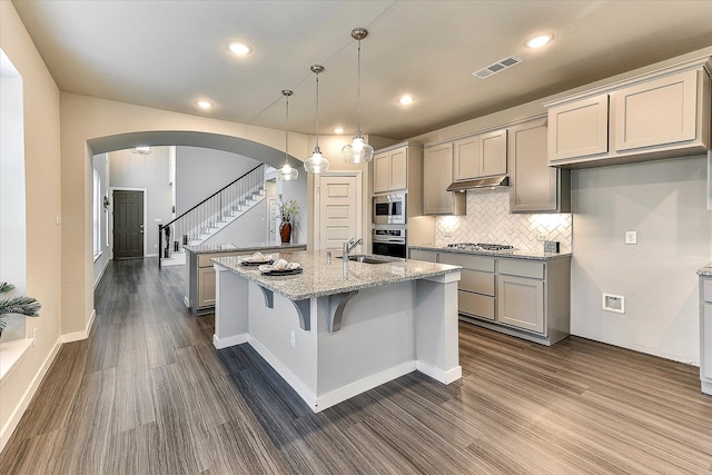 kitchen with a kitchen island with sink, hanging light fixtures, dark hardwood / wood-style floors, light stone counters, and stainless steel appliances