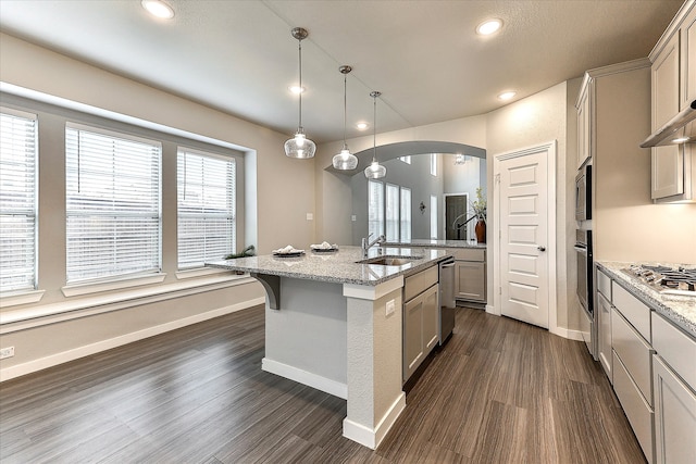 kitchen featuring sink, light stone counters, dark hardwood / wood-style floors, an island with sink, and pendant lighting