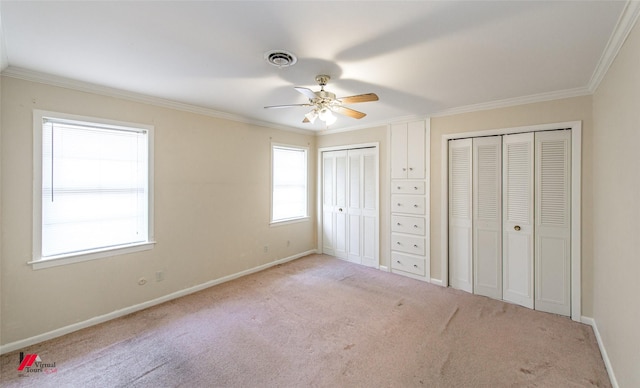 unfurnished bedroom with ceiling fan, crown molding, light carpet, and two closets