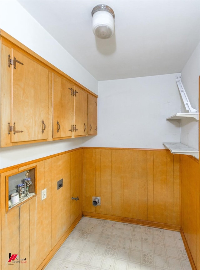 laundry area with electric dryer hookup, cabinets, and wooden walls