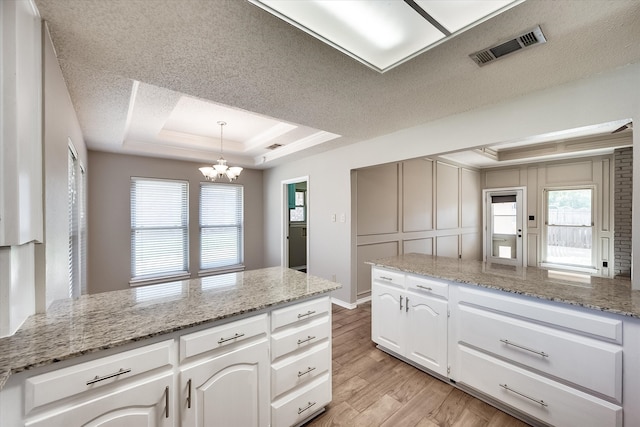 kitchen featuring white cabinets, light hardwood / wood-style flooring, light stone countertops, a tray ceiling, and a chandelier