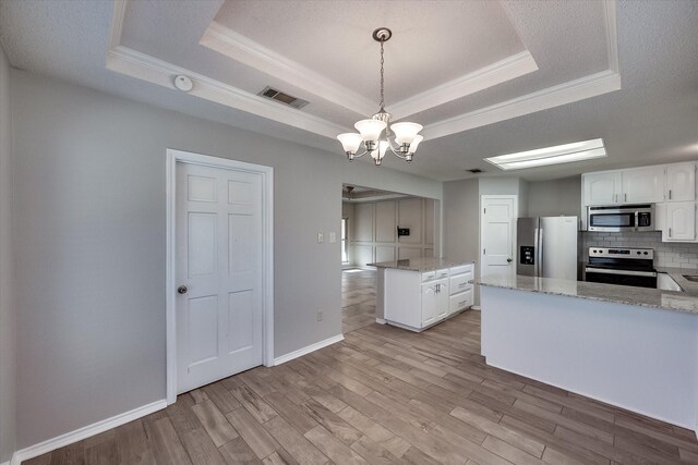 kitchen featuring hanging light fixtures, a tray ceiling, tasteful backsplash, white cabinetry, and stainless steel appliances